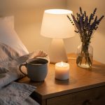 Scène de chambre apaisante le soir avec une tasse de tisane, une couverture en lin, une bougie éteinte et un vase de lavande séchée sur une table en bois.